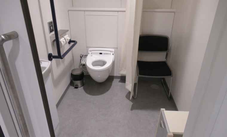 カーテンと介助を受ける人が待てる椅子を設置した男女共用トイレの写真